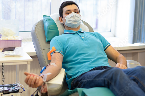 bone marrow donation. man in medical mask, male hand holding red ball, blood transfusion system, blood bag. soft focus