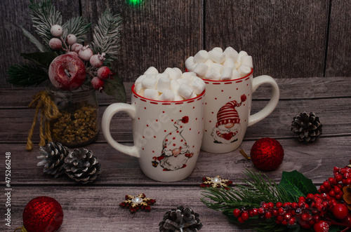 a couple of mugs with a fragrant drink with small marshmallows, an atmosphere of warmth and comfort, candles and fir branches