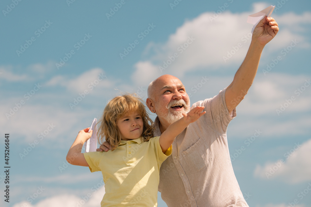Grandfather and grandson with paper plane over blue sky and clouds. Men generation granddad and grandchild. Grandfather and grandson with paper plane over blue sky and clouds. Men generation granddad and grandchild.