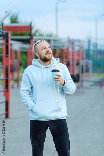 A man with a braid hairstyle in the early morning drinks coffee on the sports ground