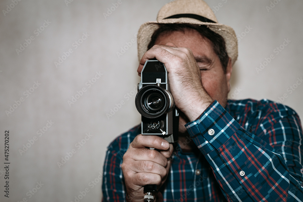 Man with Camera.cameraman make film on a retro camera.man with a plaid shirt filming with a Super 8 camera indoors.Closeup,toned,selective focus,copy space.Gray background. Man with Camera.cameraman make film on a retro camera.man with a plaid shirt filming with a Super 8 camera indoors.Closeup,toned,selective focus,copy space.Gray background.