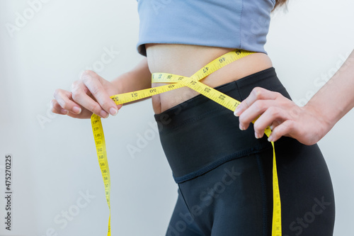 Workout, Slim asian young woman, girl standing, hand in measuring tape around waist her in fit sportswear on white background. Sport strong person in gym fitness for wellbeing, health and copy space.