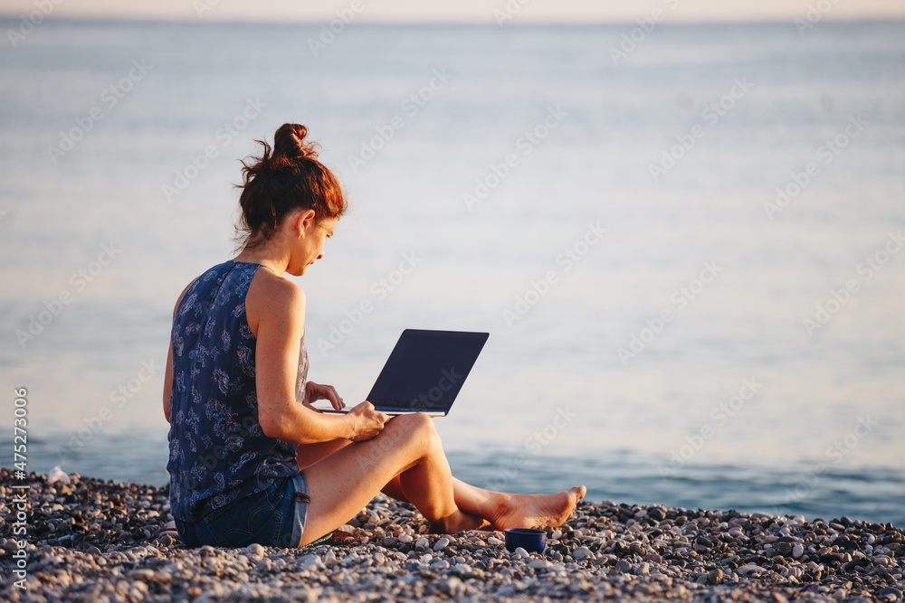 Working outdoors. Freelance concept. Technology and travel. Pretty young woman using laptop on the beach