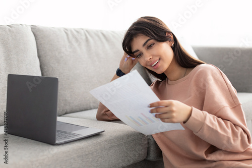 Manager holding paper reading report working on laptop at home