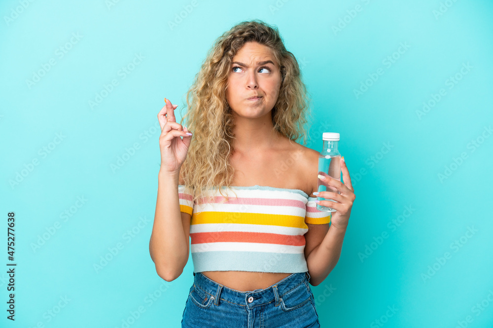 Young blonde woman with a bottle of water isolated on blue background with fingers crossing and wishing the best Young blonde woman with a bottle of water isolated on blue background with fingers crossing and wishing the best