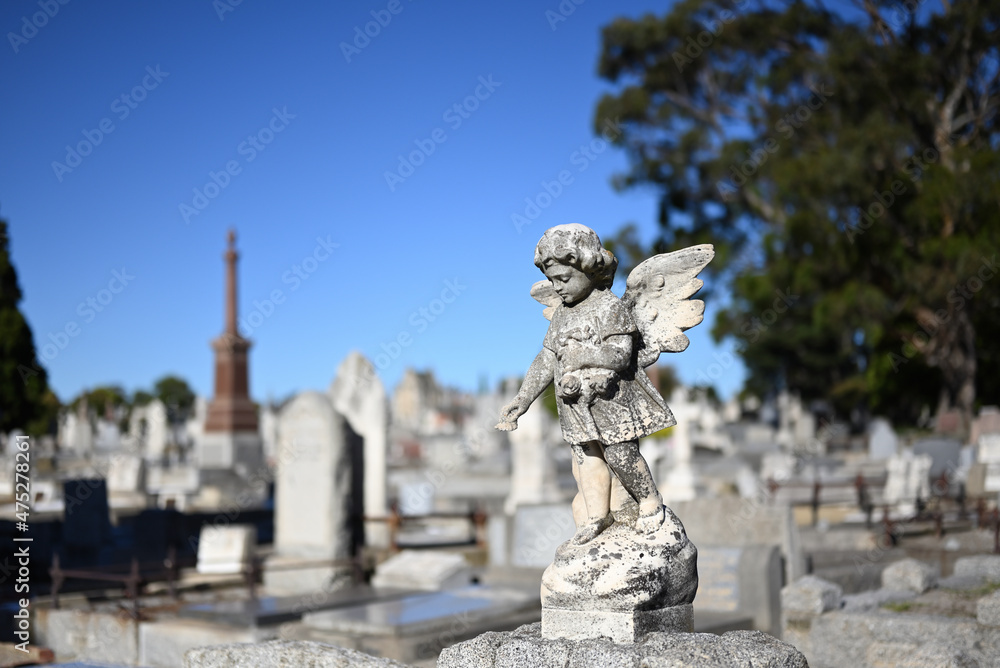Stone sculpture of an infant angel, or cherub, mournfully scattering flowers in a cemetery on a sunny day