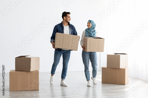 Cheerful muslim family holding moving supplies in empty apartment