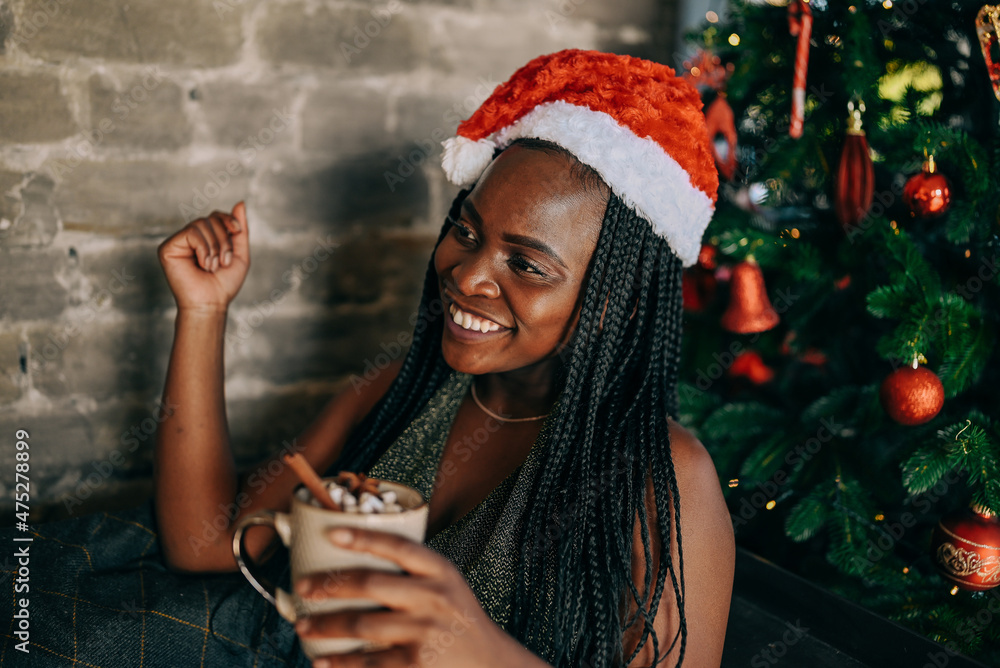 Christmas celebration, woman sits in an armchair with a cup mug of coffe or chocolate nearby decorated Christmas tree