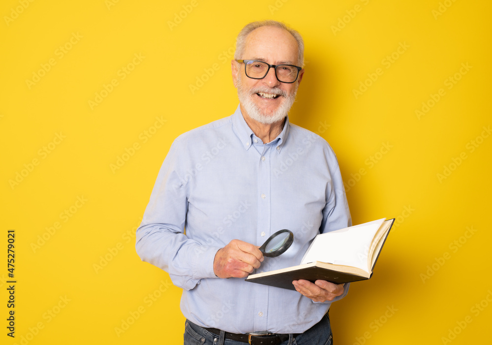 Smiling senior man reading a book isolated over yellow background. Smiling senior man reading a book isolated over yellow background.