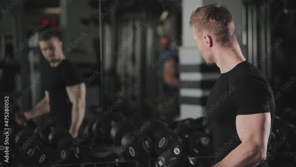A sporty man is performing a bicep exercise and alternating lifts dumbbells. He is looking in the mirror and monitoring the correct execution of the exercise. 4K A sporty man is performing a bicep exercise and alternating lifts dumbbells. He is looking in the mirror and monitoring the correct execution of the exercise. 4K