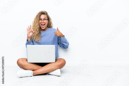 Girl with curly hair with a laptop sitting on the floor showing ok sign and thumb up gesture © luismolinero