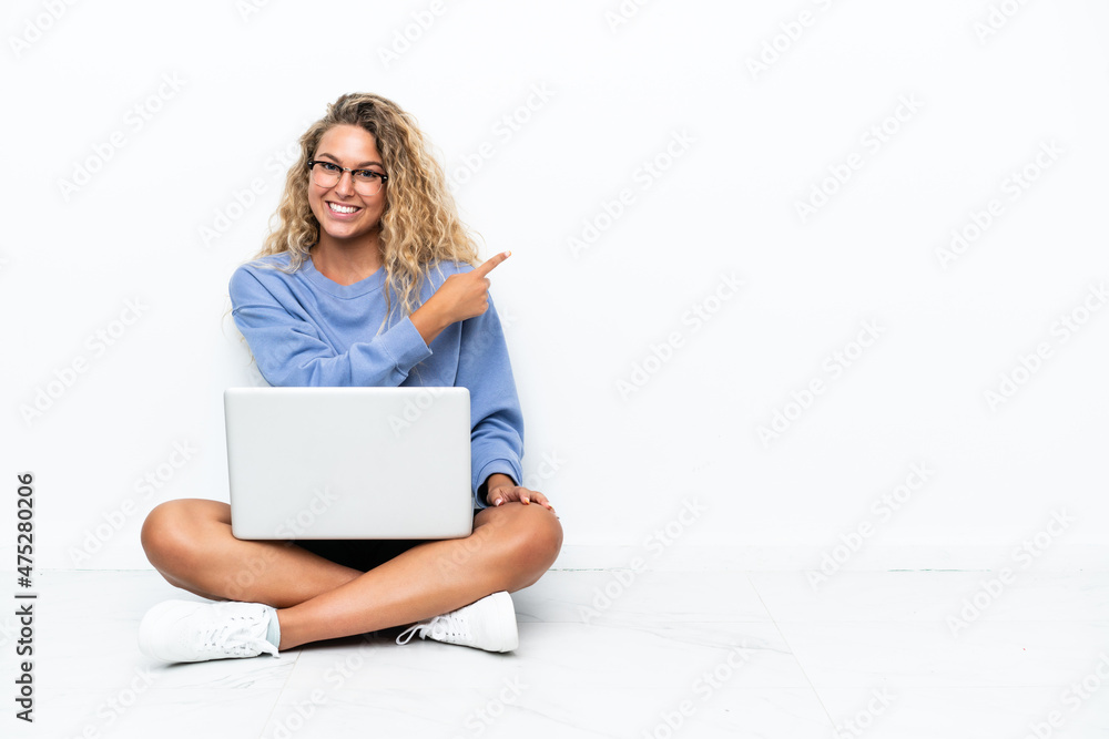 Girl with curly hair with a laptop sitting on the floor pointing back Girl with curly hair with a laptop sitting on the floor pointing back