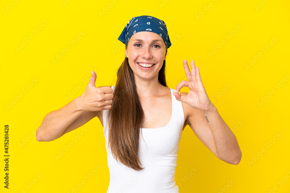 Young English woman isolated on yellow background showing ok sign and thumb up gesture Young English woman isolated on yellow background showing ok sign and thumb up gesture