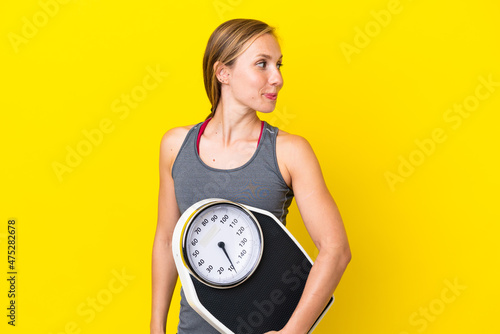 Young English woman isolated on yellow background with weighing machine