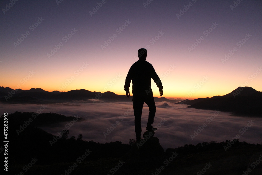 Silhueta de homem durante o nascer do sol com mar de nuvens ao fundo 