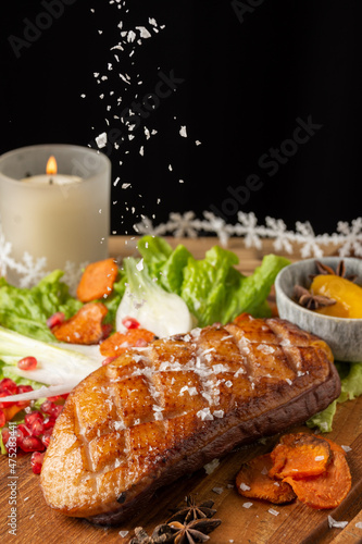 Top view of duck breast with falling salt, lettuce, chives and peaches, on table with vel and Christmas decoration, black background, vertical