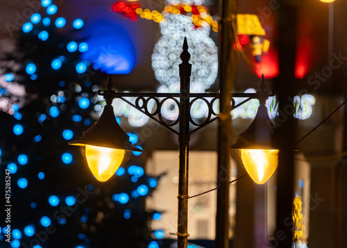 Vintage retro style double high street shopping lights. Lamps with Christmas decorations illuminated and snowman lit up behind out of focus.