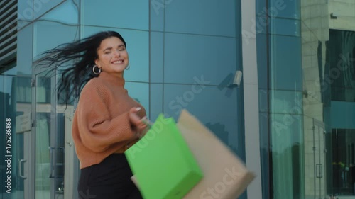 Happy hispanic girl rejoices new purchases bought on sale with discount in shop young woman smiling walking down street with gift packages confident gait joyful lady whirls merrily enjoying life
