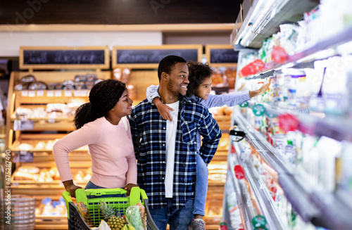 Schilderij op canvas Portrait of happy black family with trolley shopping together at grocery store