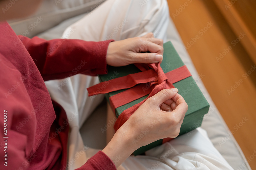 Christmas eve festival season day, hands of young woman, girl holding green gift box with red ribbon, bow on sofa. Happy to get received present on merry xmas. Celebration on New Year festival people.