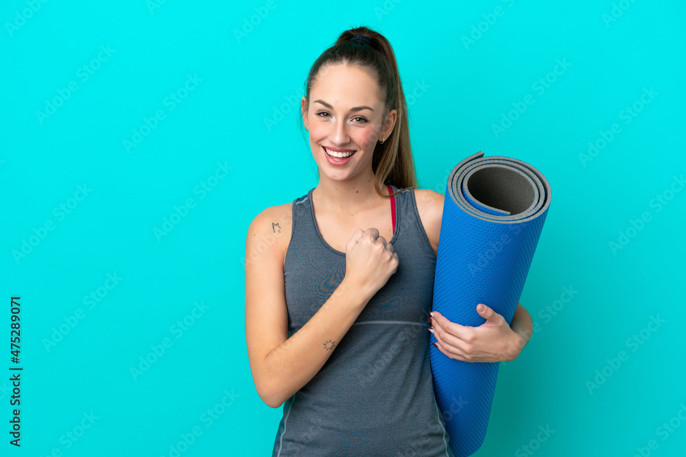 Young sport caucasian woman going to yoga classes while holding a mat isolated on blue background celebrating a victory Young sport caucasian woman going to yoga classes while holding a mat isolated on blue background celebrating a victory