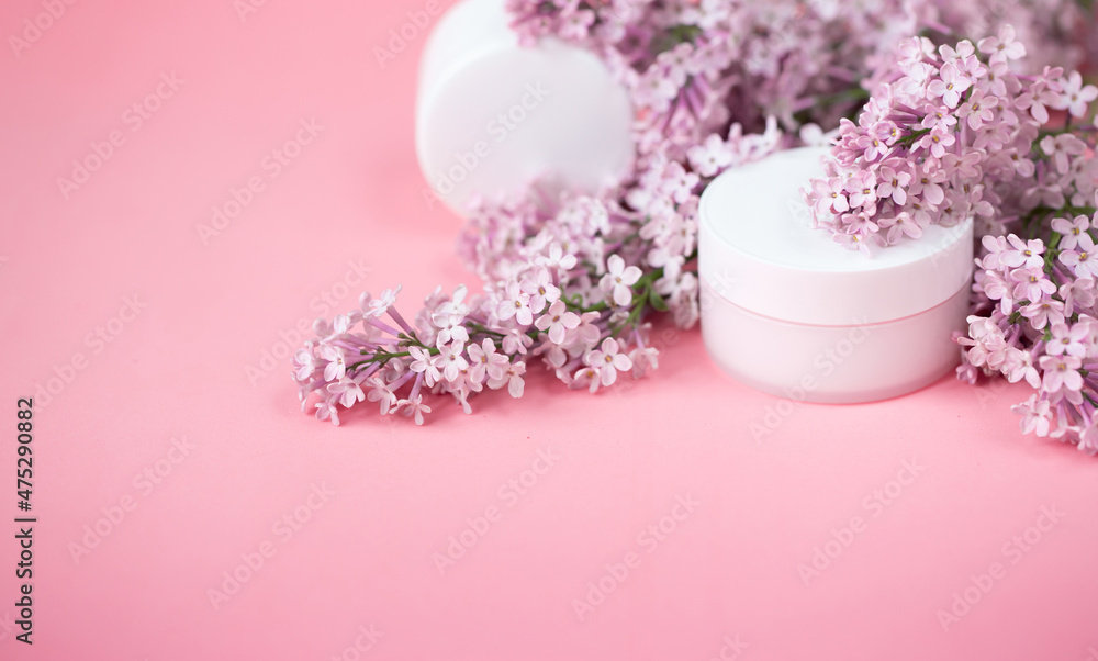 Face and body skin care. A set of cosmetic creams and balms in white tubes and cans on a coral background with sprigs of lilac flowers. Spa treatments for home care. Home rejuvenation and moisturizing Face and body skin care. A set of cosmetic creams and balms in white tubes and cans on a coral background with sprigs of lilac flowers. Spa treatments for home care. Home rejuvenation and moisturizing