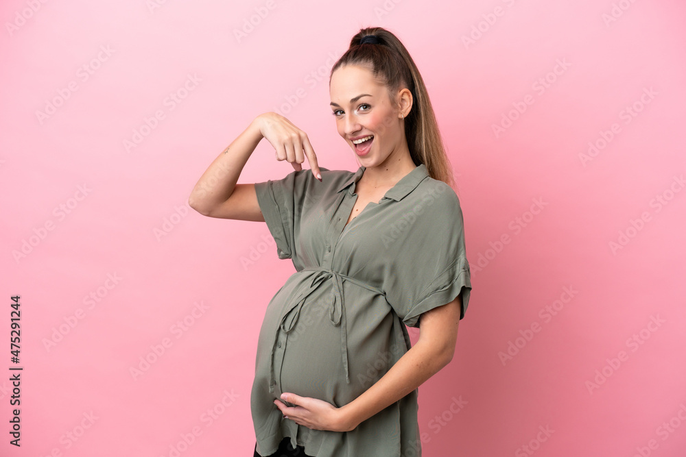 Young woman isolated on pink background pregnant and pointing to the belly Young woman isolated on pink background pregnant and pointing to the belly