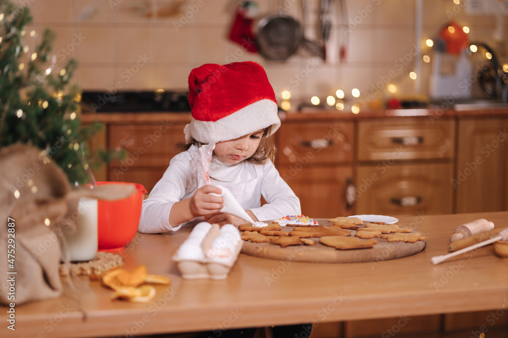 Little girl in santa hat decorates gingerbread using multicolored beads. Christmas and New Year traditions concept. Christmas bakery. Happy hollidays Little girl in santa hat decorates gingerbread using multicolored beads. Christmas and New Year traditions concept. Christmas bakery. Happy hollidays