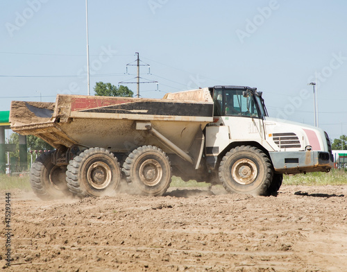 articulated dump truck in motion, driving along a dusty road. Construction machine in the process of transporting soil at a construction site