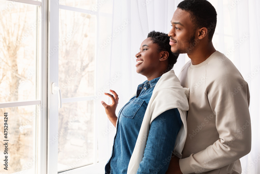 Black couple standing near glass window and looking Black couple standing near glass window and looking