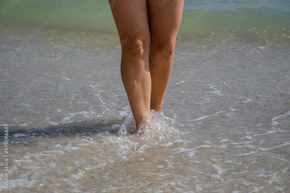 Women's feet walk on sea water on a sunny summer day. Relaxation and wellness concept