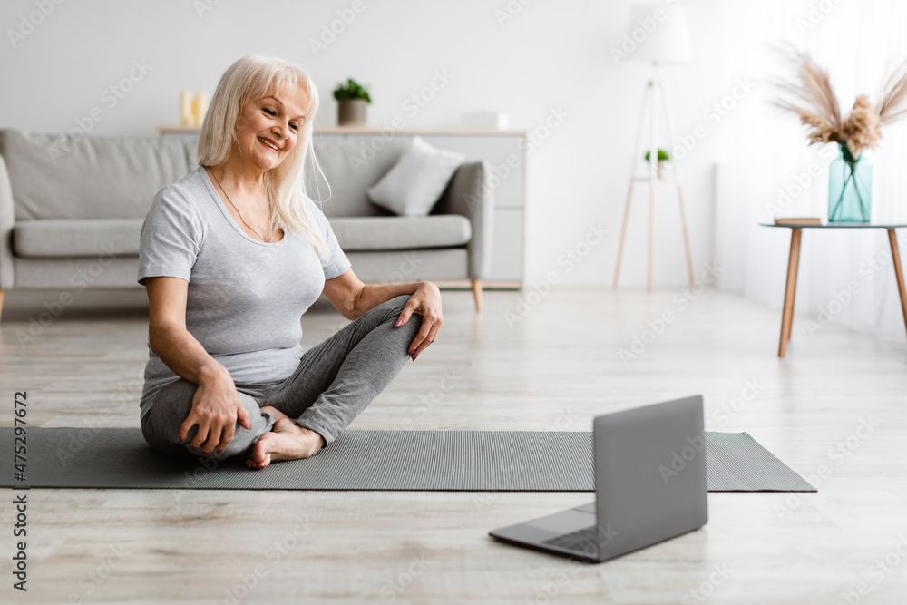 Mature woman exercising at home watching online tutorial on laptop