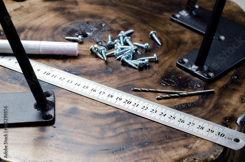 Roulette and pencil. Screws on the table in the workshop. The hands of a wood master. Metal table legs. Desktop. Working process. Furniture creation.