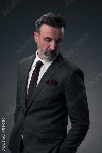 Portrait of a stylish elegant senior businessman with a beard and casual business clothes in photo studio isolated on dark background gesturing with hands © .shock