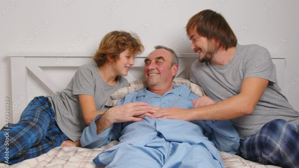 Aged male patient embracing kids and talking while lying on bed at home Aged male patient embracing kids and talking while lying on bed at home