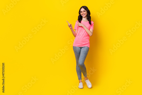 Full length photo of young pretty girl indicate fingers empty space promo ads isolated over yellow color background