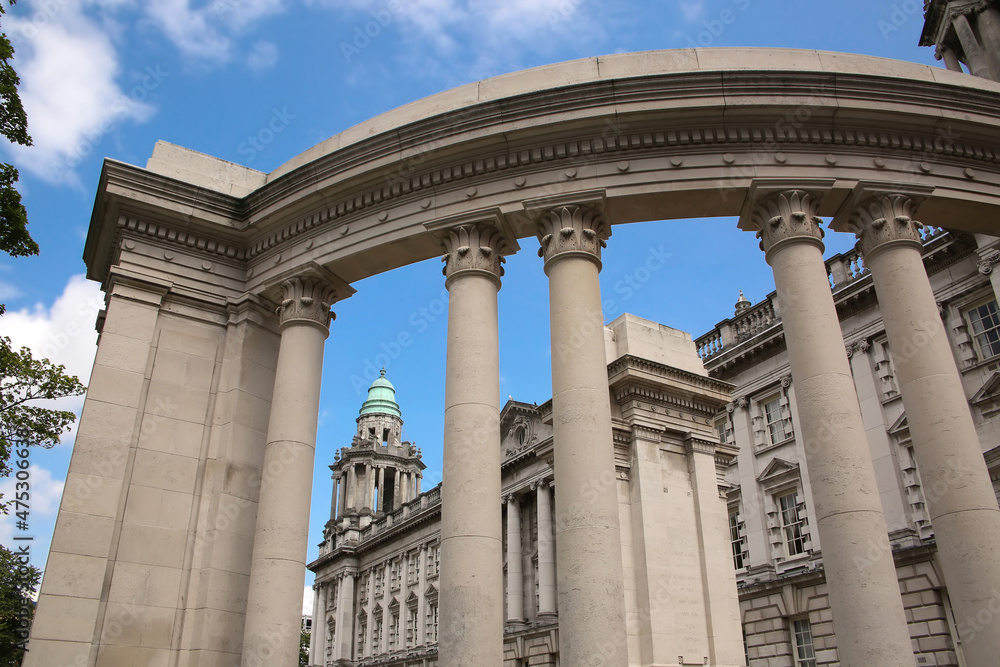 Belfast City Hall building with a classical Renaissance stone exterior and corner tower with columns.  Semi circular monument with columns in front.  Donegall Square, Belfast, Northern Ireland.