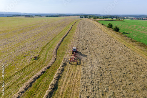 Aerial view on a tractor that collects hay in rows with a disc rake. Farmer stores fodder for cattle in summer season.