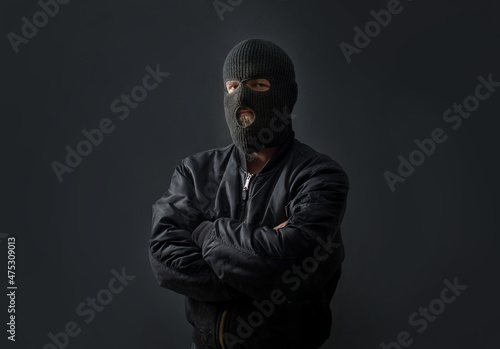 Obraz na plátne a man stands against a dark background in a black bomber jacket and a balaclava