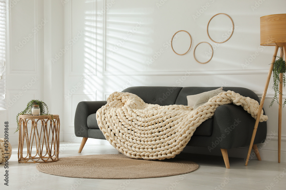Fototapeta premium Soft chunky knit blanket on sofa in living room. Interior design
