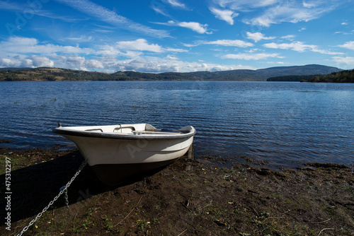 A white old wooden boat anchored near the shore, in a secluded harbor. Landscape photography of a beautiful blue lake and an anchored white boat.