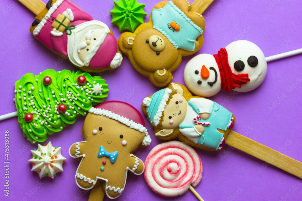 Cookies on sticks in a shape of Santa Claus, elf character, Gingerbread man, snowman, bear, New Year 2022 tree, lollipop on purple background top view. Cute treats, sweets, candies for Christmas fun. Cookies on sticks in a shape of Santa Claus, elf character, Gingerbread man, snowman, bear, New Year 2022 tree, lollipop on purple background top view. Cute treats, sweets, candies for Christmas fun.