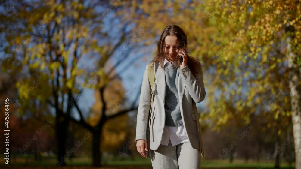 woman with mobile phone is walking in park in autumn sunny day, calling and chatting woman with mobile phone is walking in park in autumn sunny day, calling and chatting