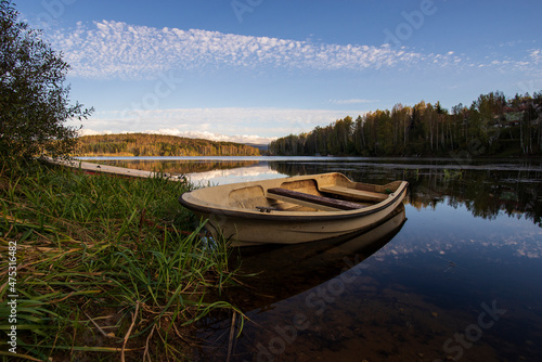 A white old wooden boat anchored near the shore, in a secluded harbor. Landscape photography of a beautiful blue lake and an anchored white boat.