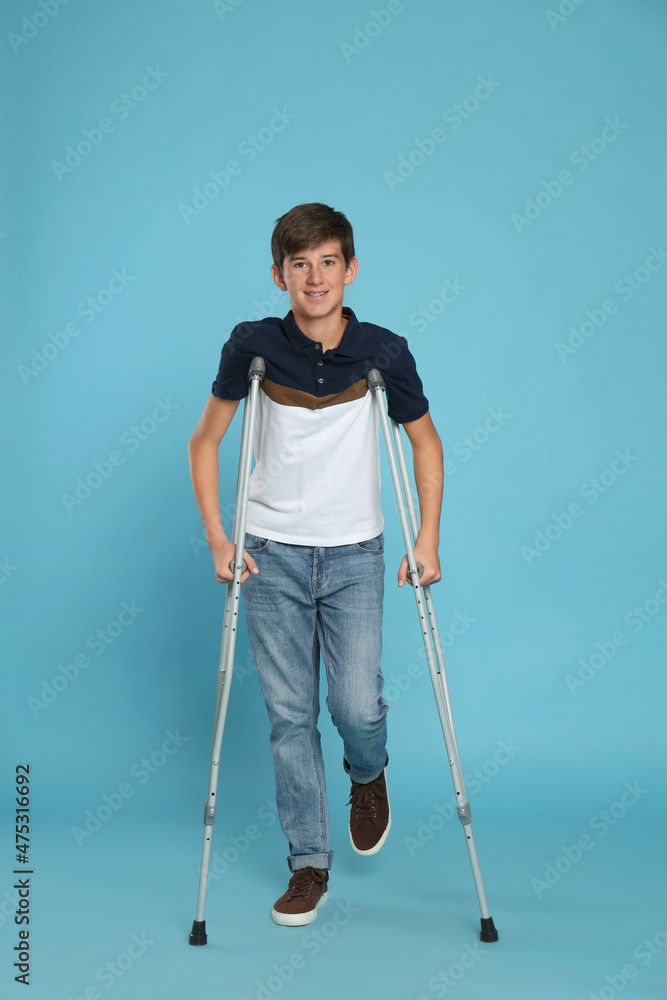 Teenage boy with injured leg using crutches on turquoise background Teenage boy with injured leg using crutches on turquoise background