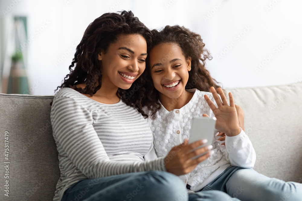 Smiling black mother and daughter having video call on smartphone