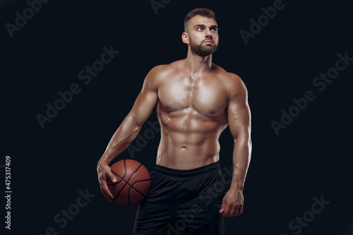 Portrait of a very muscular naked man playing basketball isolated on black background