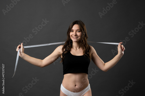Woman in a black top and white panties with a white measuring tape, in a black background. Healthy lifestyle concept. Diet.