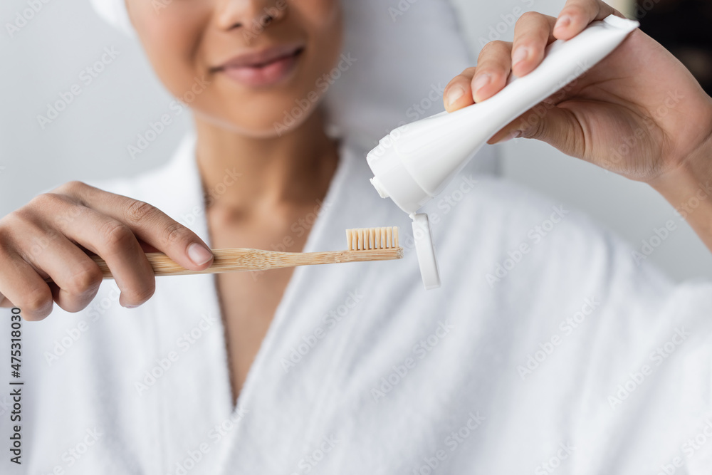 cropped view of blurred african american woman in bathrobe holding toothpaste and toothbrush in bathroom cropped view of blurred african american woman in bathrobe holding toothpaste and toothbrush in bathroom