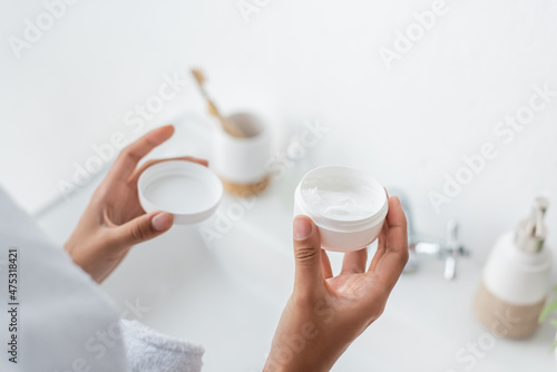 cropped view of african american woman holding container with face cream in bathroom